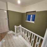 gloss white painted bannisters against an olive green wall showing top landing