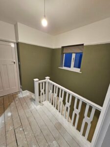 gloss white painted bannisters against an olive green wall showing top landing